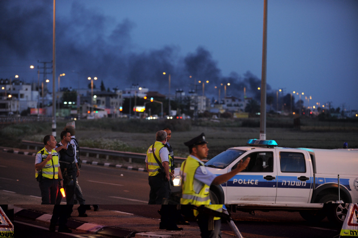 Policemen block the entrance road to the Arab city Tayibe as smoke rises from the city