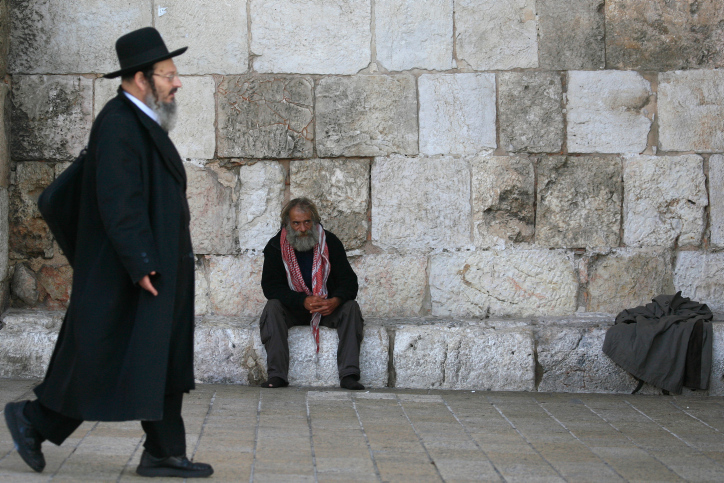 Palestinian man resting in the Old City of Jerusalem while an Ulrta Orthodox Jew walks by