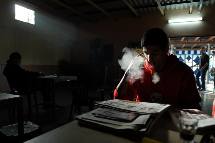 A young Arab man is drinking coffee, reading newspaper and smoking nargila in a traditional Arab coffee shop in  Ajami, Jaffa's Arab neighbourhood