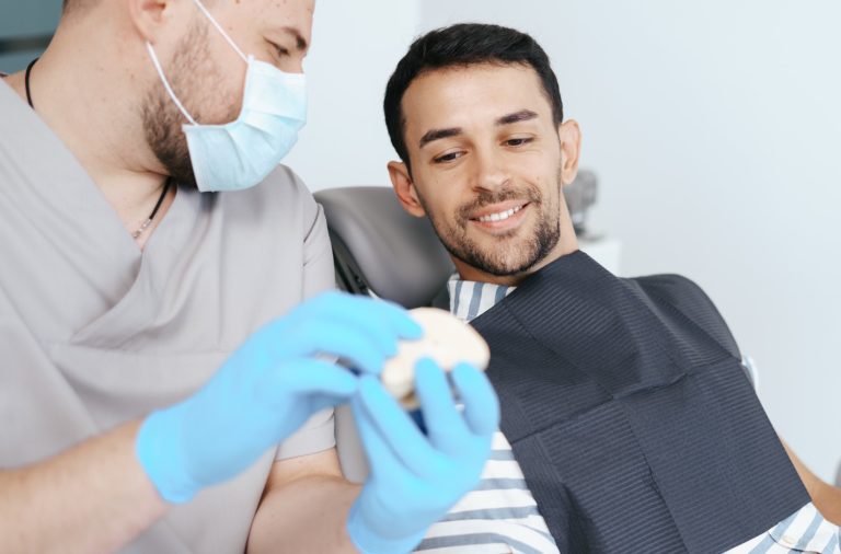 male-dentist-medical-mask-explaining-artificial-teeth-smiling-patient-clinic
