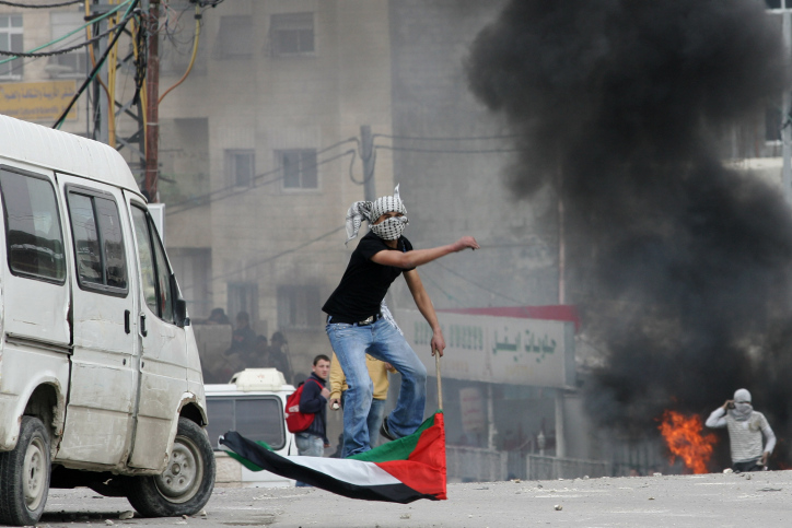 A Palestinian youth throws stones towards Israeli troops