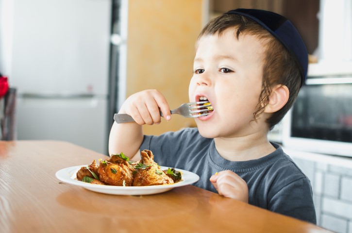 a child in a t-shirt in the kitchen eating an omelet, a fork