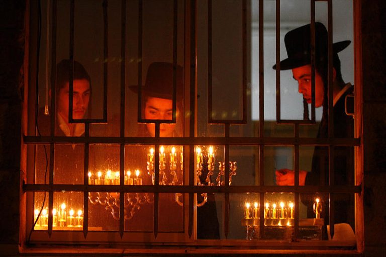 An ultra orthodox jewish man lights a candle in the traditional hanukkiya