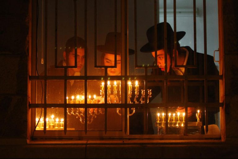 An ultra orthodox jewish man lights a candle in the traditional hanukkiya
