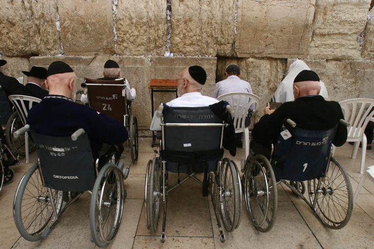Old jewish men sit in wheel chairs infront of the wailing wall