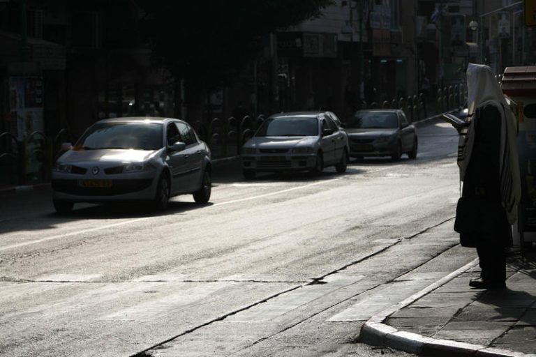 A man wearing tallit is waiting to cross the street